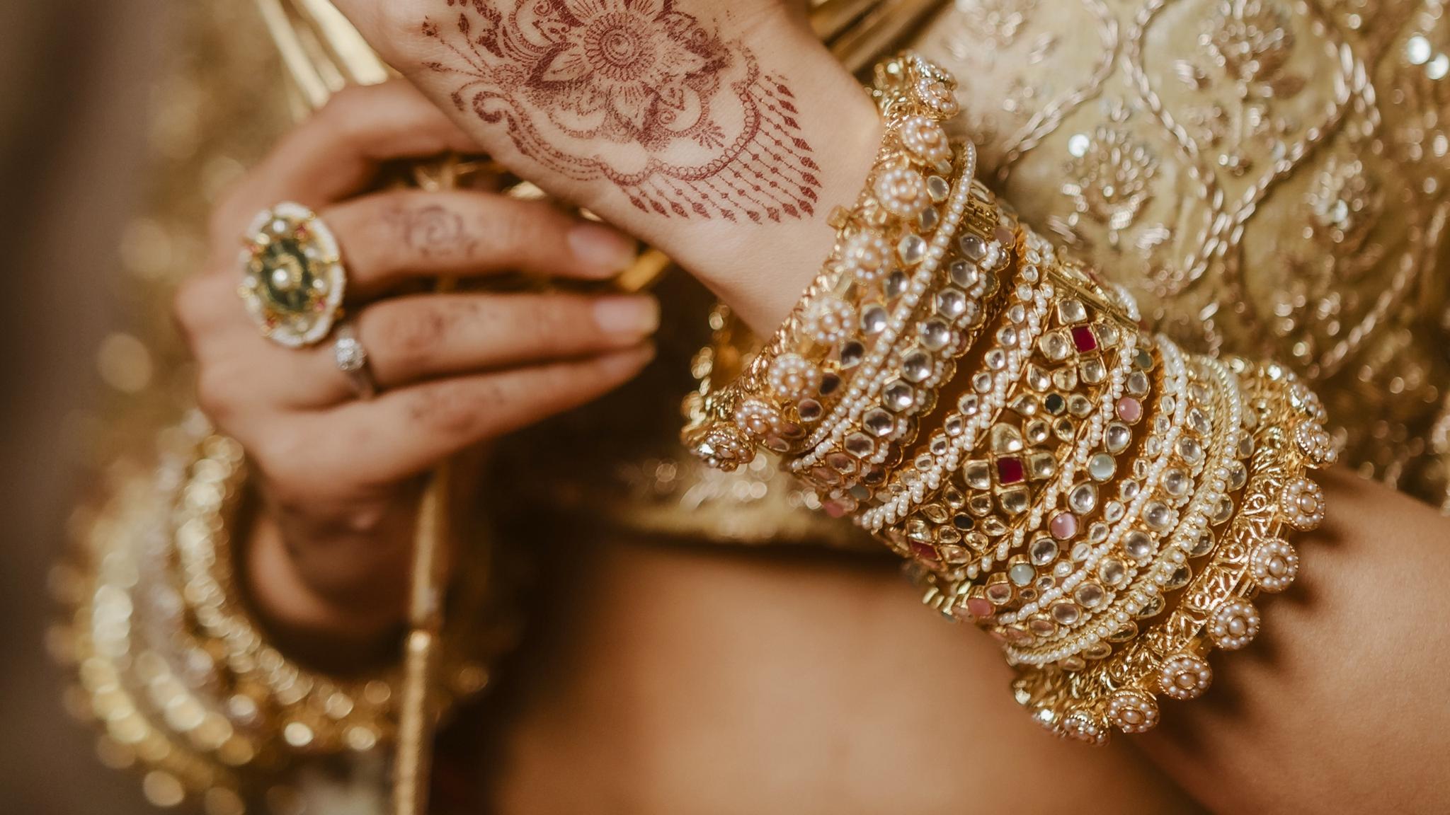 A bride's hands with mehndi, wearing gold bangles from Outbox House